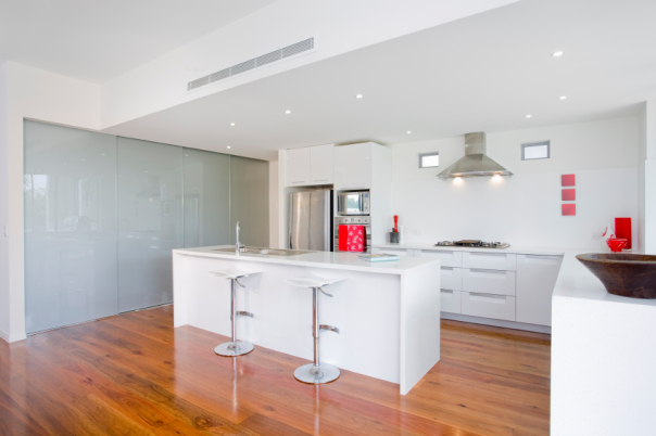 Modern kitchen with white cabinetry, marble wrap-around counter, stainless steel appliances, and wood flooring