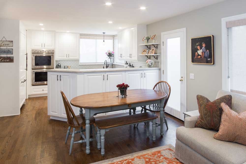 Comtemporary dining room and open kitchen with white cabinets, stainless stell appliances and oval wood dining table