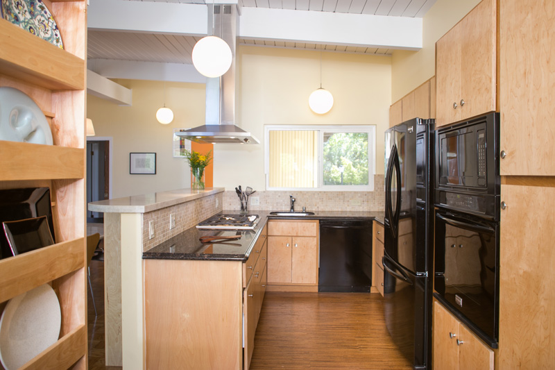 Modern kitchen with light natural wood cabinets and black appliances and countertops