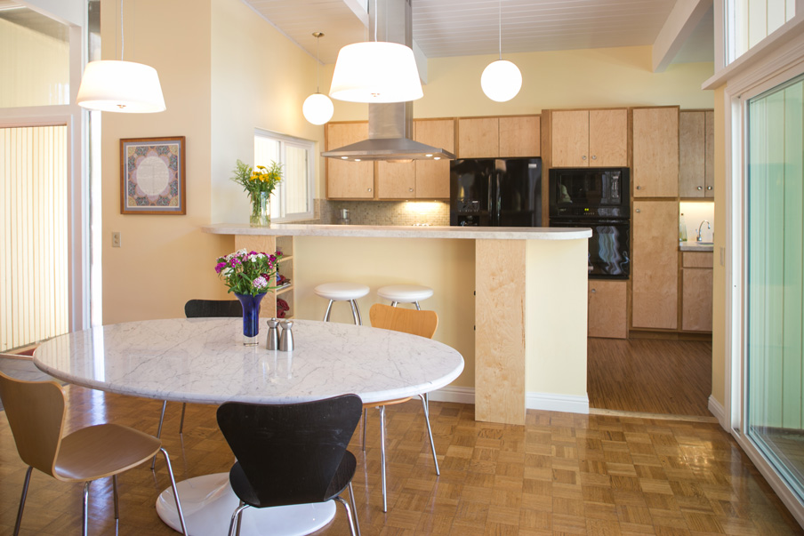 Mid-century modern dining room and kitchen with oval white table and wood floors and cabinets