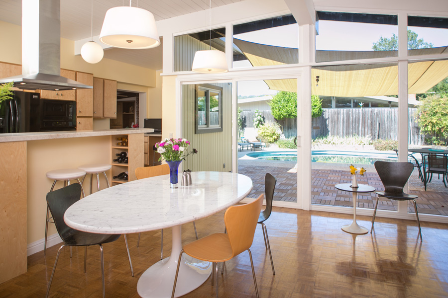 Mid-century modern open kitchen and dining area with modern white oval table and view of backyard with pool