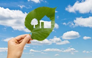 Hand holding leaf with a house cut out against blue sky