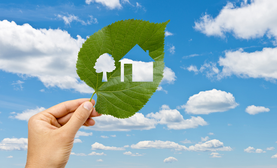 Hand holding leaf with a house cut out against blue sky