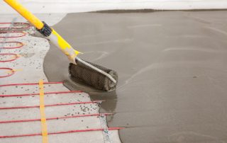 Radiant heating system installation in new house. Worker align cement with roller