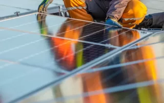 Person in orange worksuit seen from waist down installing smooth solar panel on rooftop