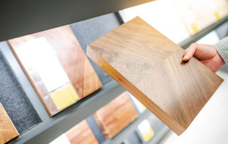 Hand holding a square of beige wood near a display rack