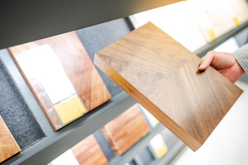 Hand holding a square of beige wood near a display rack