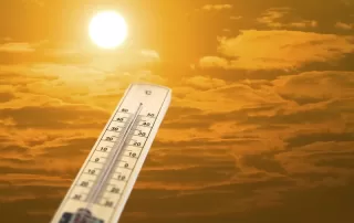 Thermometer against a yellow sky with clouds and bright sun.