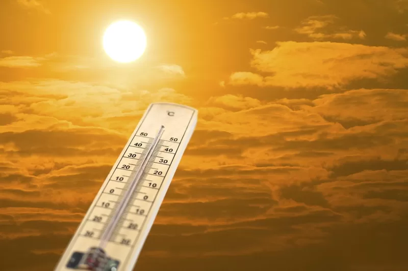 Thermometer against a yellow sky with clouds and bright sun.