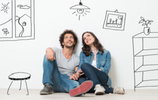 Portrait Of Happy Young Couple Sitting On Floor Looking Up While Dreaming Their New Home And Furnishing