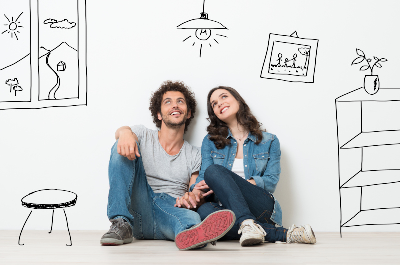 Portrait Of Happy Young Couple Sitting On Floor Looking Up While Dreaming Their New Home And Furnishing