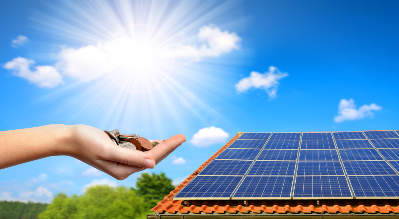 Solar panel on the roof of the house and coins in hand. The concept of money saving and clean energy.