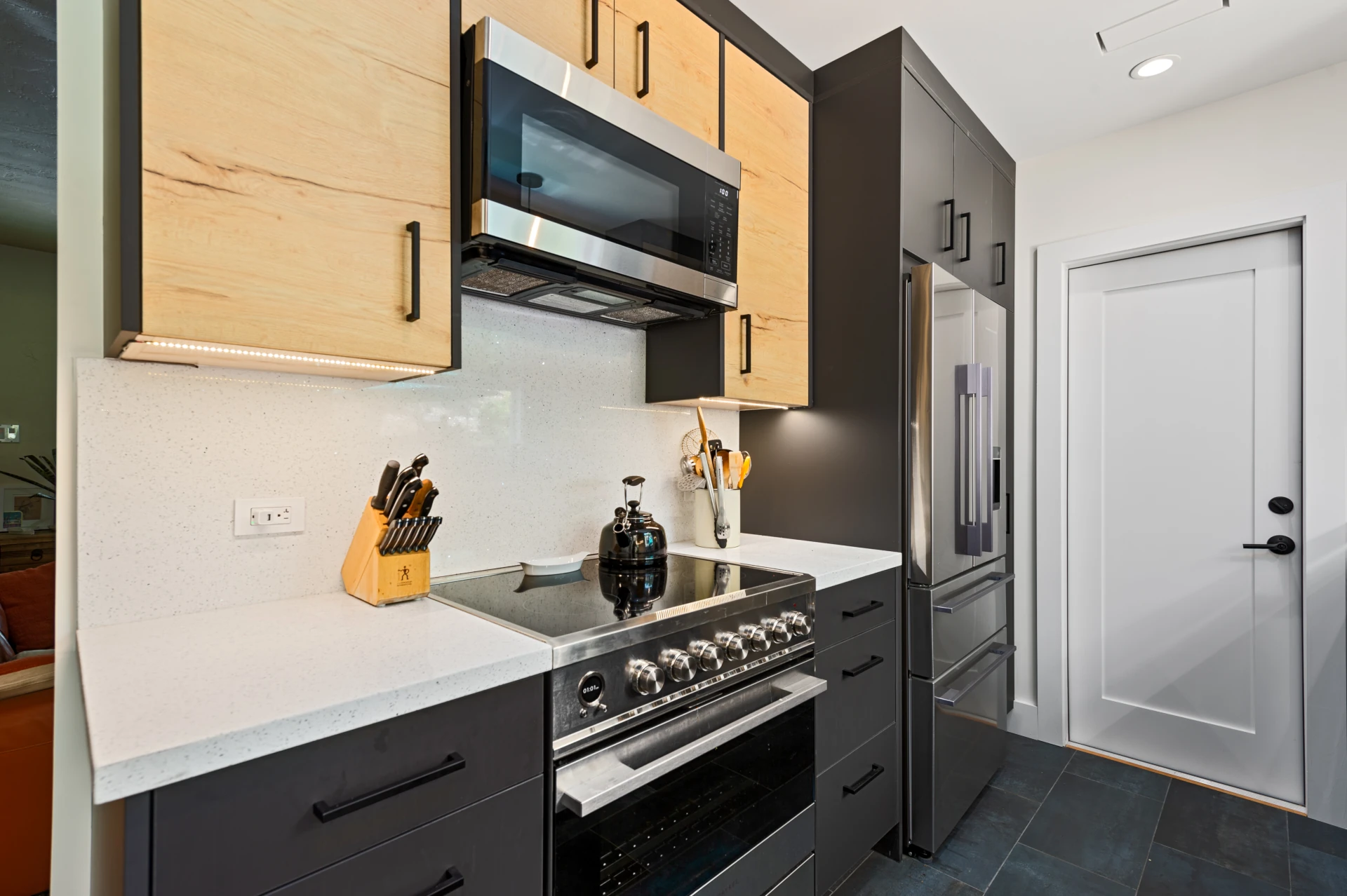 Kitchen with dark wood bottom cabinets, light wood upper cabinets, stainless-steel range and French-door refigerator, white quartz countertop and grey-green tile flooring.