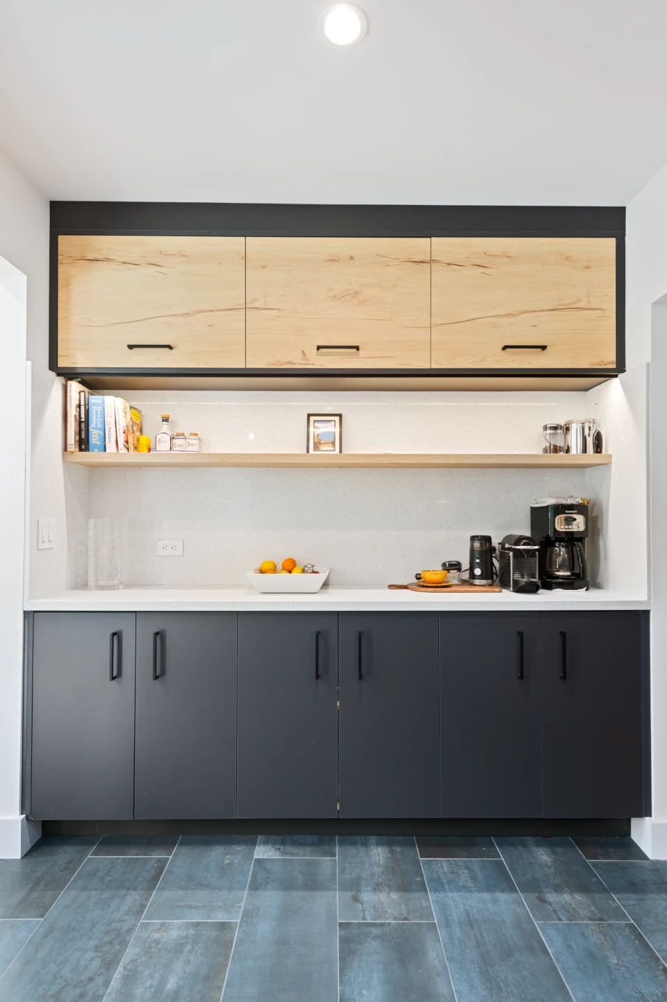 Kitchen with dark wood bottom cabinets, light wood upper cabinets, and a light wood open shelf, white quartz countertop and grey-green tile flooring.