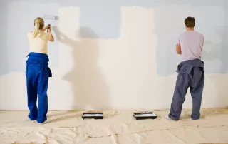 Man and woman rolling beige paint onto a light blue wall.