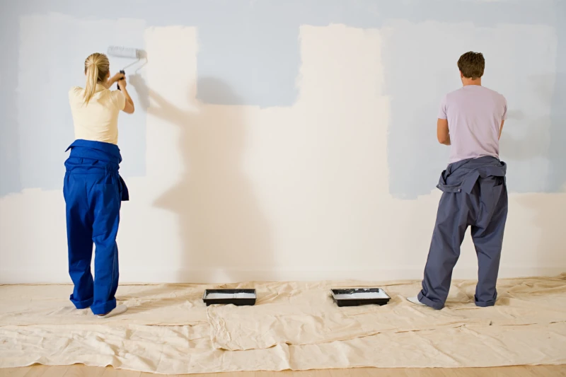 Man and woman rolling beige paint onto a light blue wall.