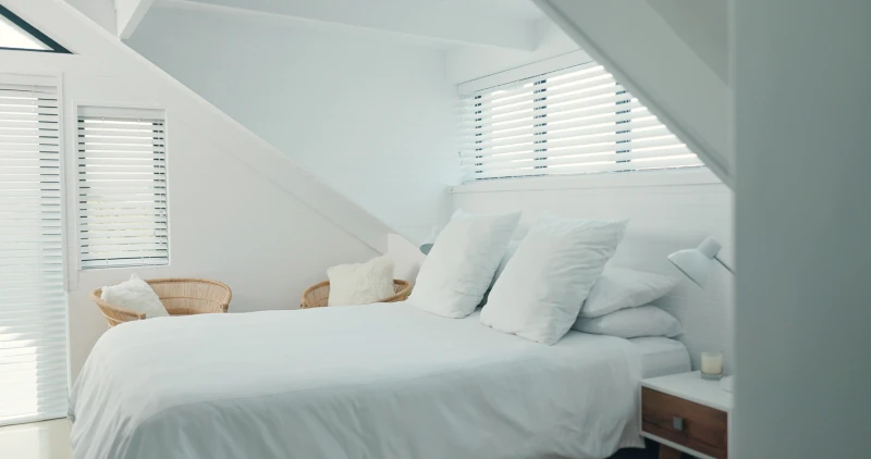 Light, airy bedroom with white walls and large bed with white sheets and pillows