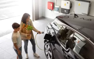 Happy son and mother plug EV charger from home charging station to electric vehicle. Eco-friendly car powered by renewable source of clean energy.